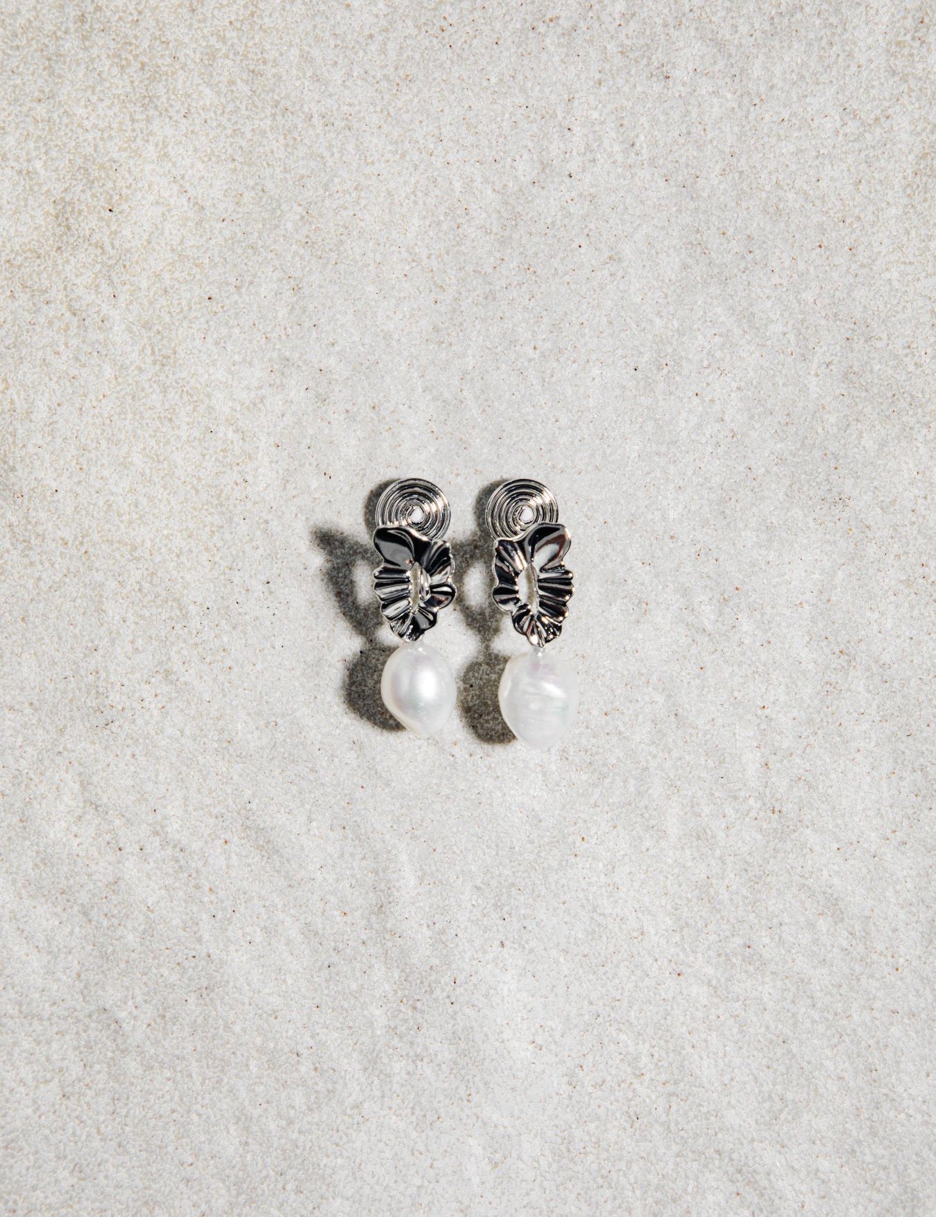 Mini Destiny Earrings in silver – clip-on pearl earrings on a textured grey background with soft natural shadows