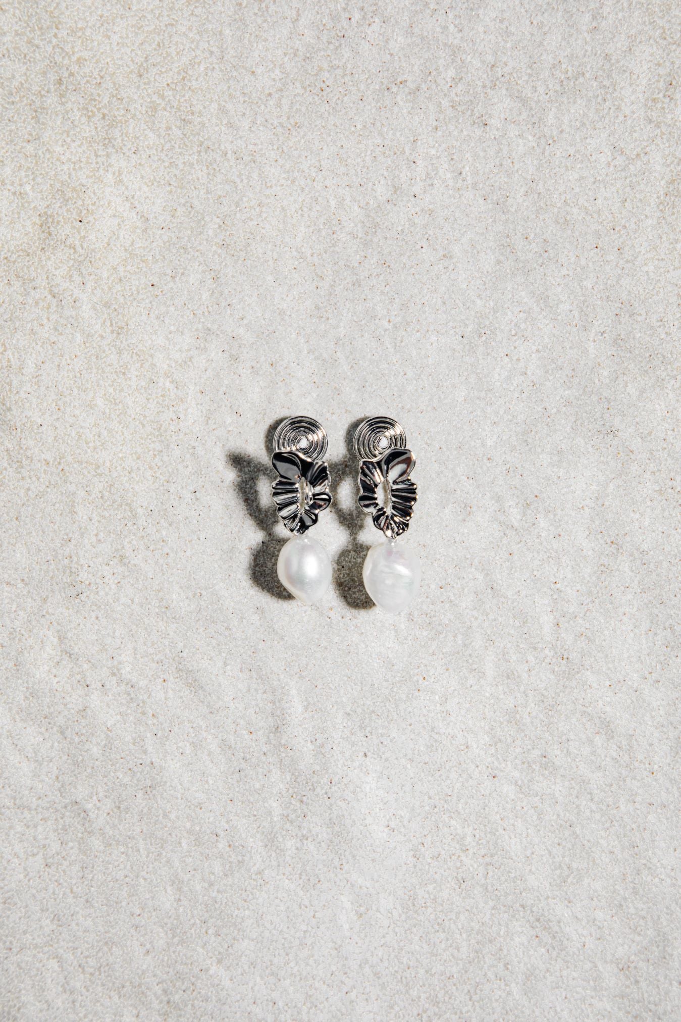Mini Destiny Earrings in silver – clip-on pearl earrings on a textured grey background with soft natural shadows