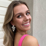 Woman smiling in pink dress wearing Ciara Earrings in silver and white crystal – soft glam look with long hair and natural light backdrop