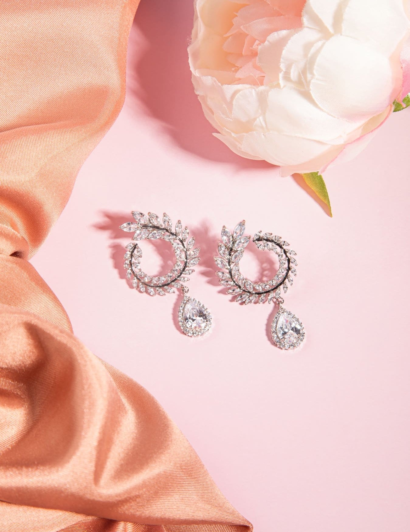 Lover’s Charm Earrings – cubic zirconia leaf hoop and teardrop earrings on blush background with satin and florals
