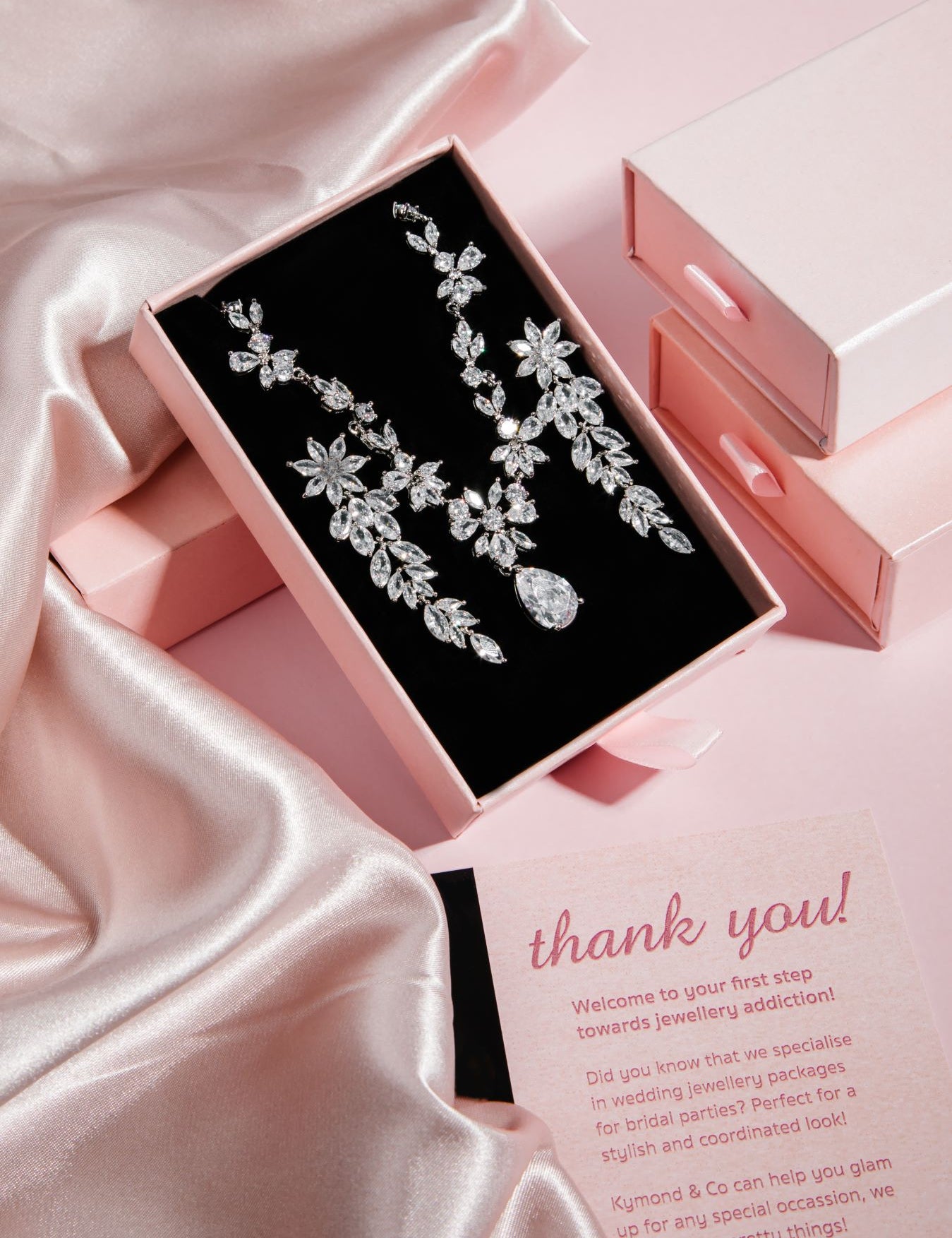 The Simone Set – platinum-plated floral necklace with teardrop cubic zirconia pendant in black velvet box, styled on pink satin background