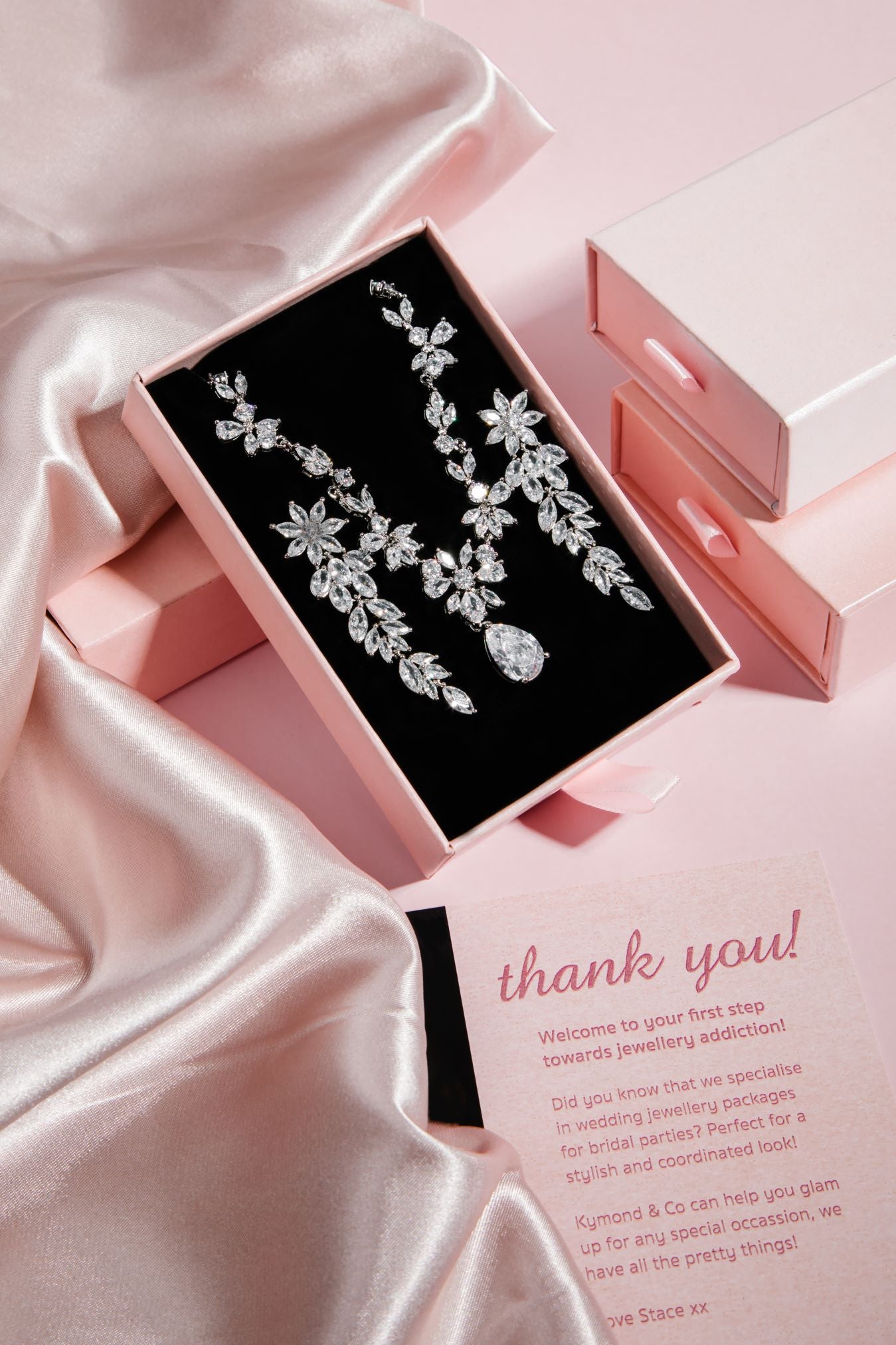 The Simone Set – platinum-plated floral necklace with teardrop cubic zirconia pendant in black velvet box, styled on pink satin background