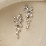 Gemma Earrings in silver – floral cubic zirconia drop earrings resting on ivory linen cloth.