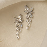 Gemma Earrings in silver – floral cubic zirconia drop earrings resting on ivory linen cloth.