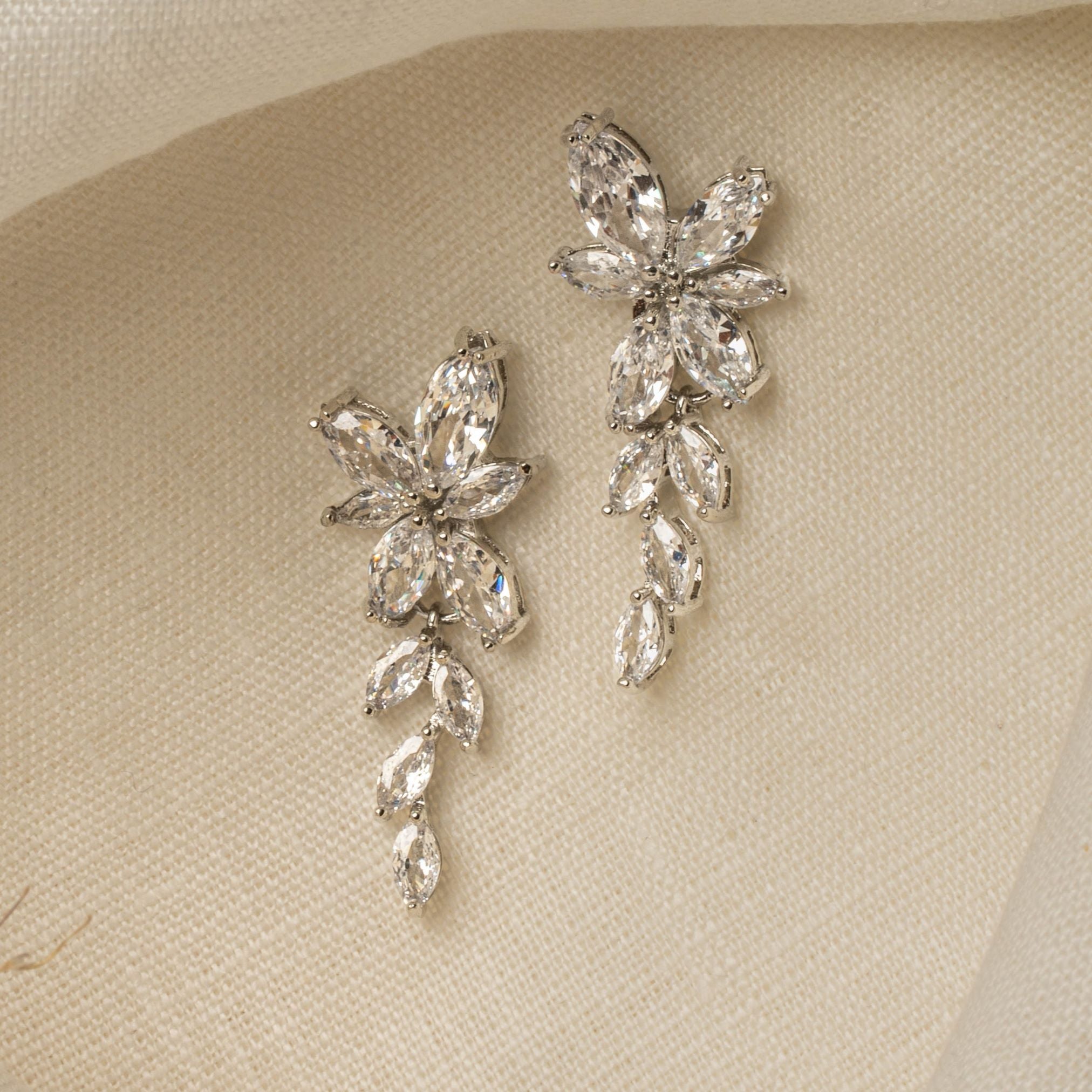 Gemma Earrings in silver – floral cubic zirconia drop earrings resting on ivory linen cloth.