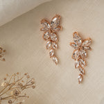 Gemma Earrings in rose gold – asymmetrical floral design photographed on linen with dried flowers.