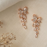 Gemma Earrings in rose gold – asymmetrical floral design photographed on linen with dried flowers.