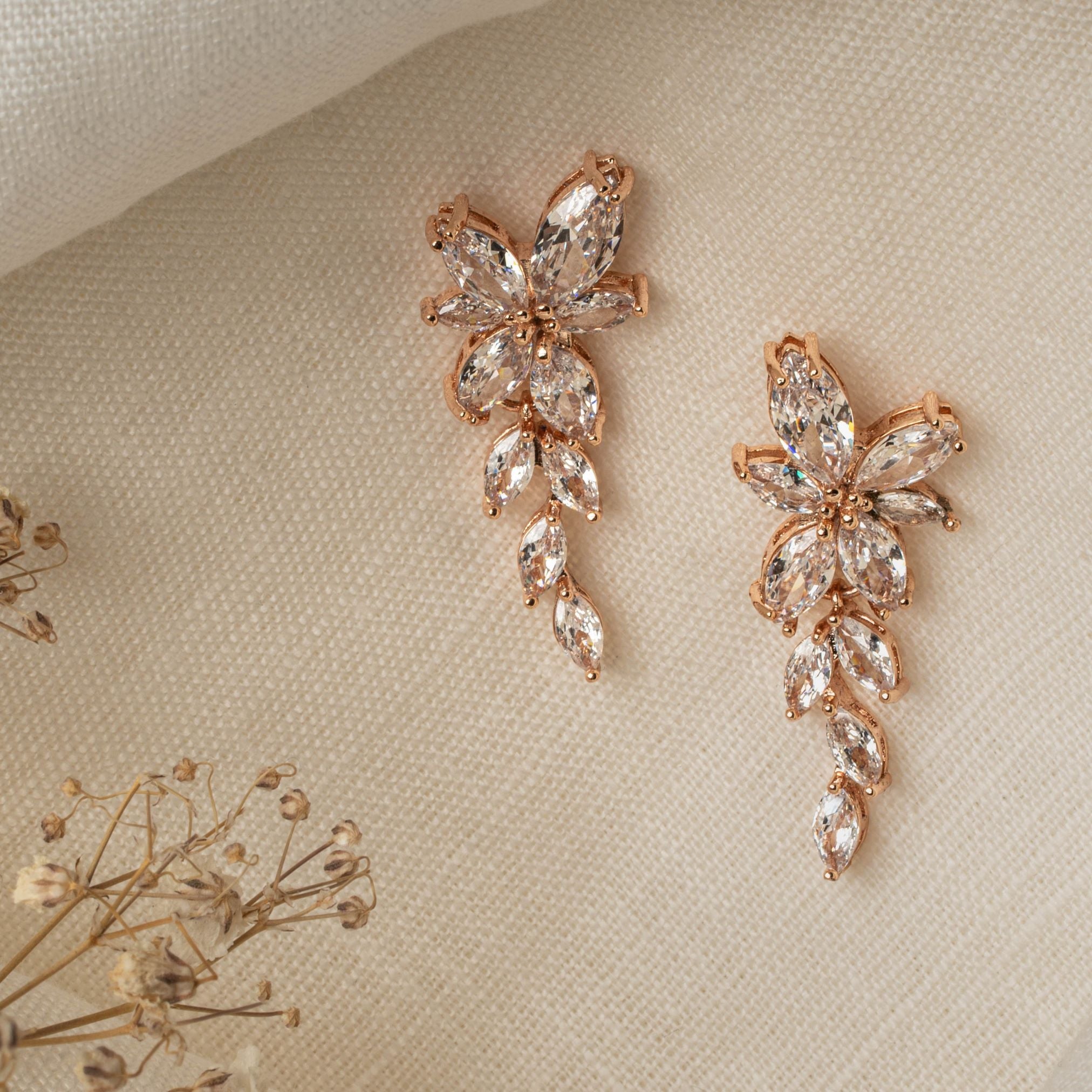 Gemma Earrings in rose gold – asymmetrical floral design photographed on linen with dried flowers.