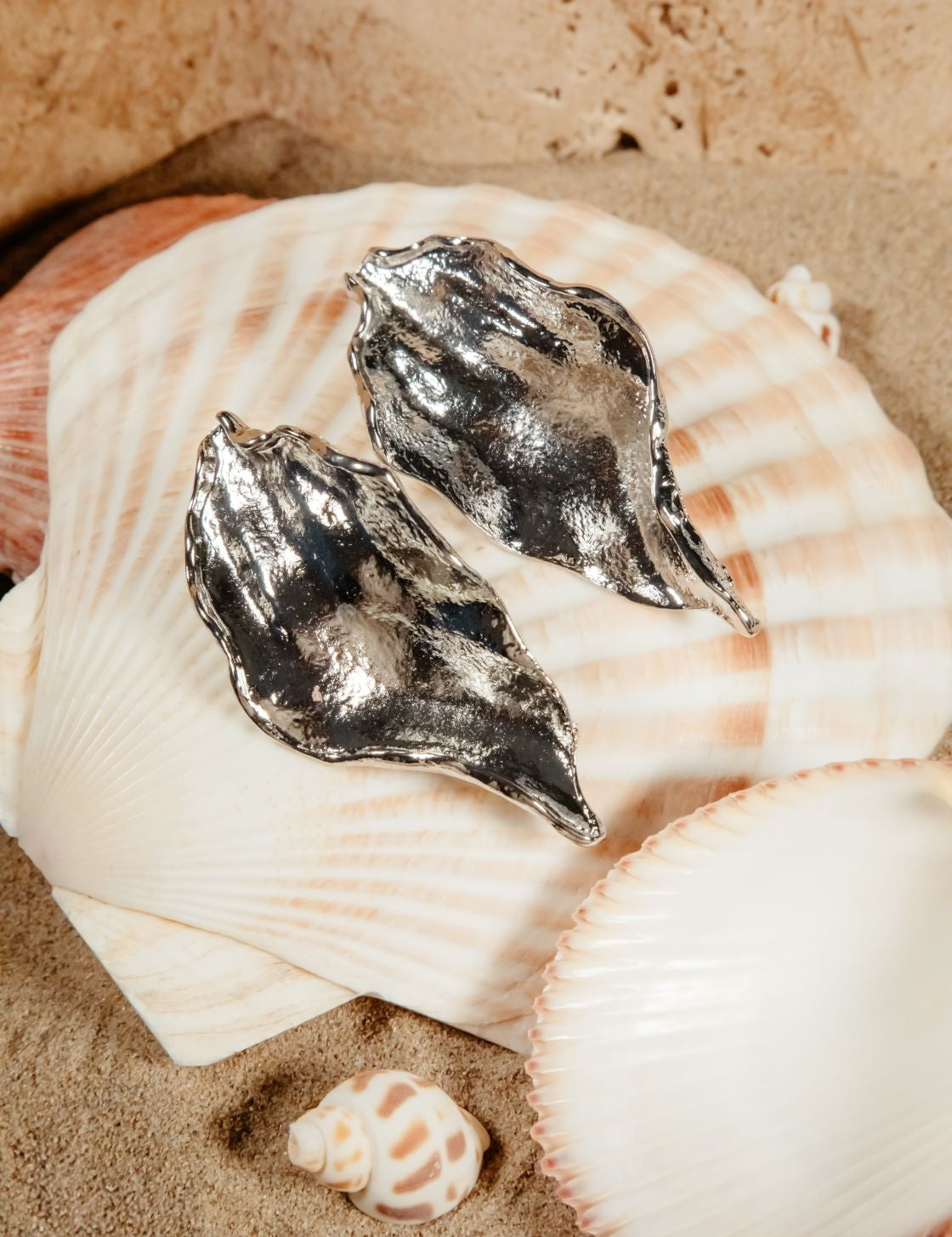 Silver Lucia Earrings styled in beach flatlay – resting on clamshells with natural shell scatter over soft sand